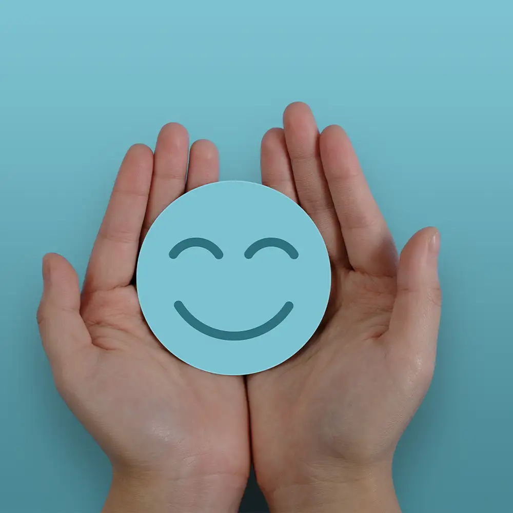 Ein blaues fröhliches Smiley wird von zwei Händen gehalten