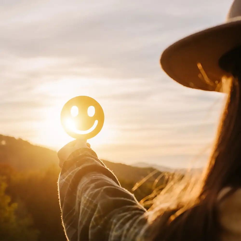 Hände halten einen zufriedenen Smiley aus Pappe gegen das Sonnenlicht